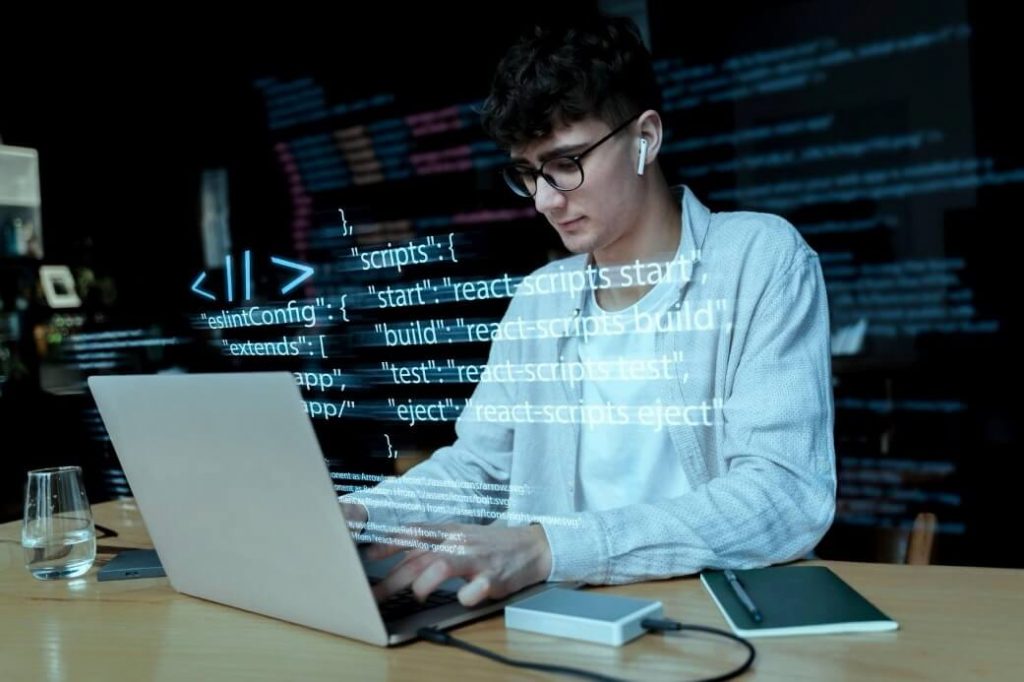 молодой парень в очках за ноутбуком работает в техподдержке хостинг провайдера и предотвращает утрату ценной информации